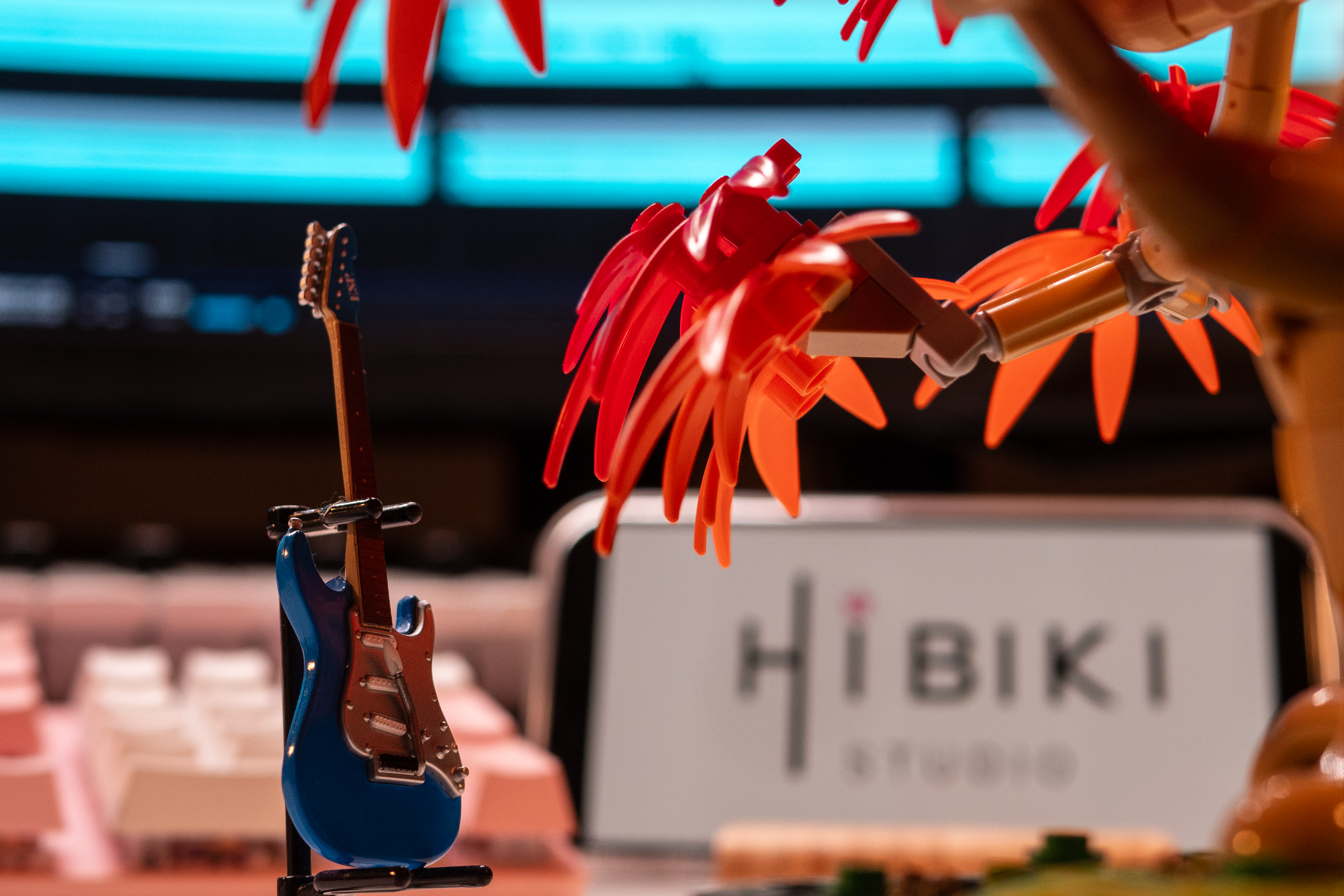 A close shot to a guitar sit under a maple tree, which both are figurines on the desk, with a HIBIKI Studio logo behind.